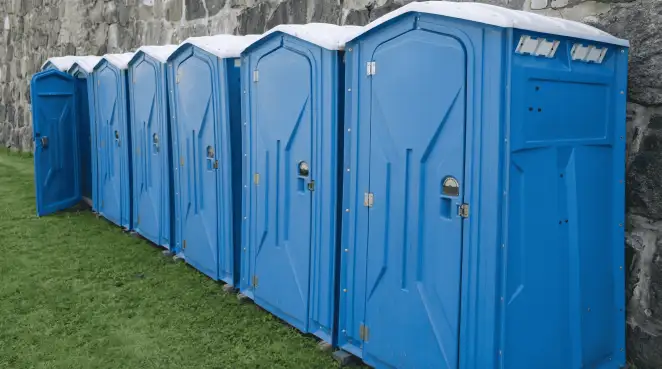 Row of blue portable toilets lined up on grass against a stone wall for event sanitation in Sacramento, CA