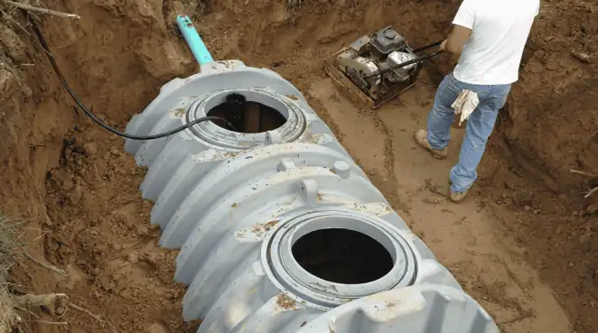 Septic tank installation showing a technician compacting soil around a new poly septic tank in an excavation pit in Sacramento, CA